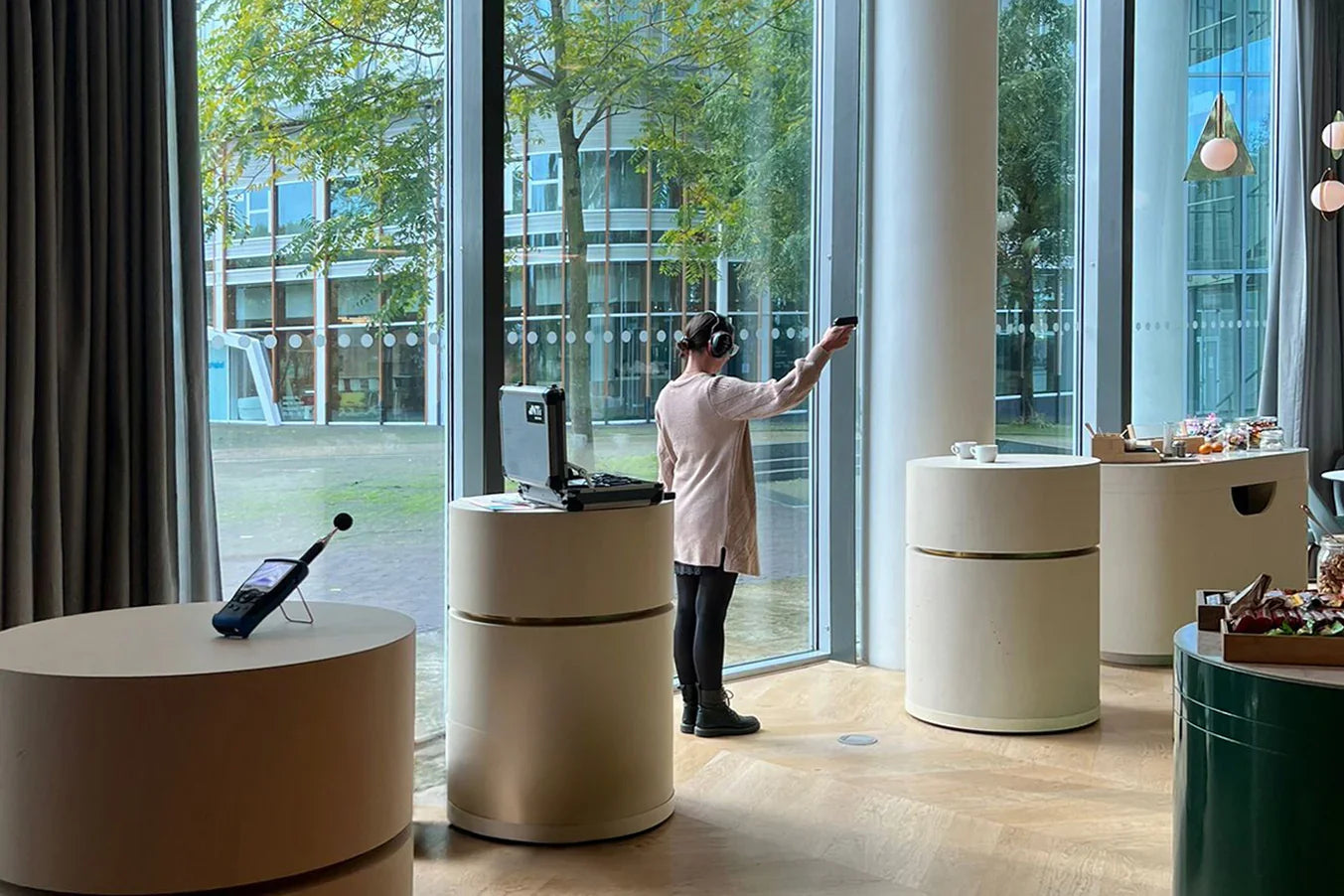 Akoestische meting in modern kantoor met grote ramen, ronde meubels en kantoormeubilair.