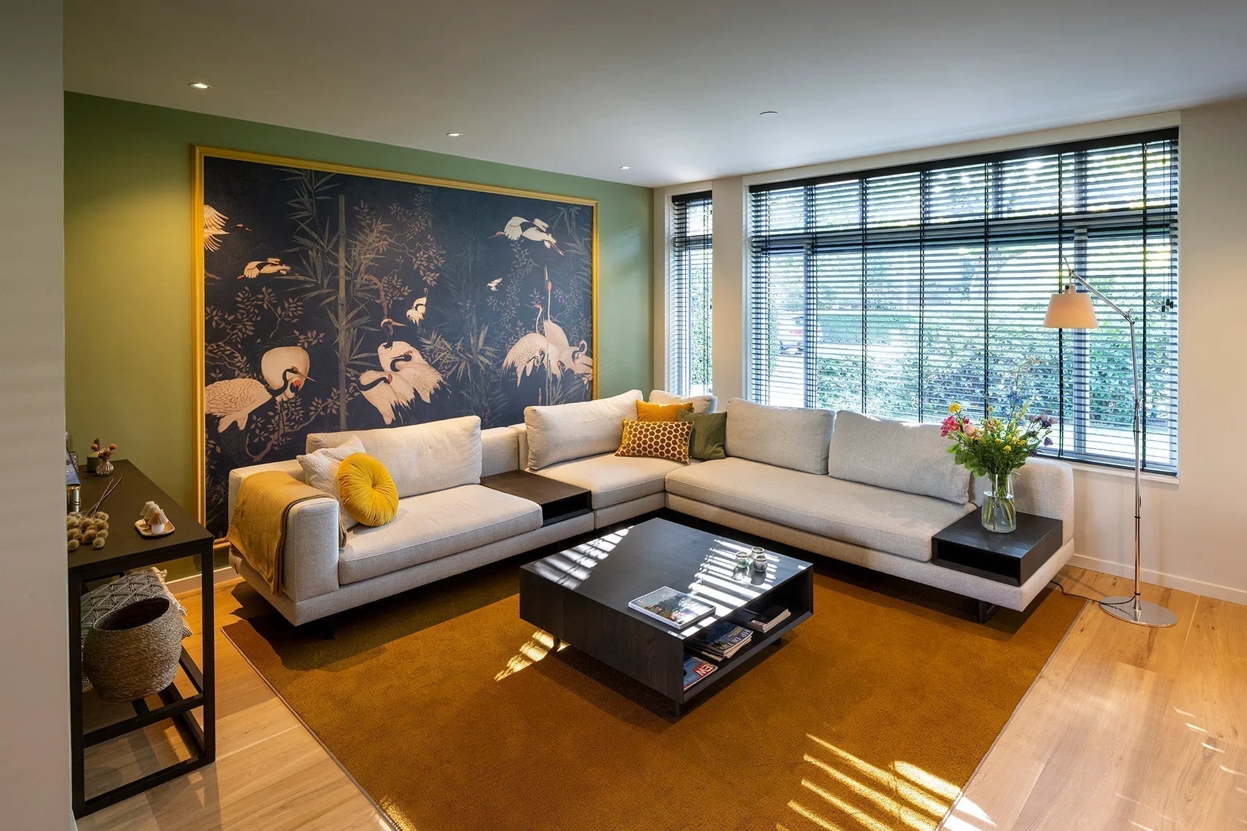 Modern woonkamer met grote lichtgrijze hoekbank, geel vloerkleed en muurschildering met vogels
