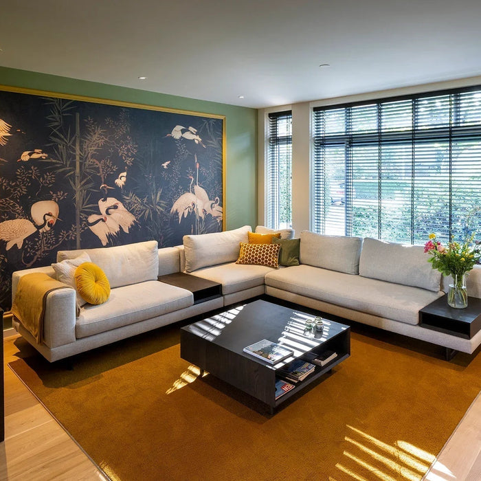 Modern woonkamer met grote lichtgrijze hoekbank, geel vloerkleed en muurschildering met vogels