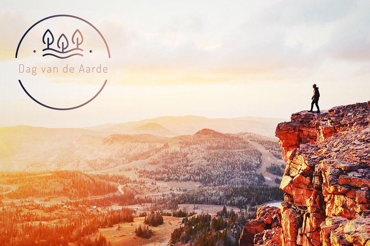 Persoon op rots met uitzicht op berglandschap bij zonsopkomst, Dag van de Aarde logo linksboven.