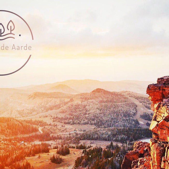 Persoon op rots met uitzicht op berglandschap bij zonsopkomst, Dag van de Aarde logo linksboven.