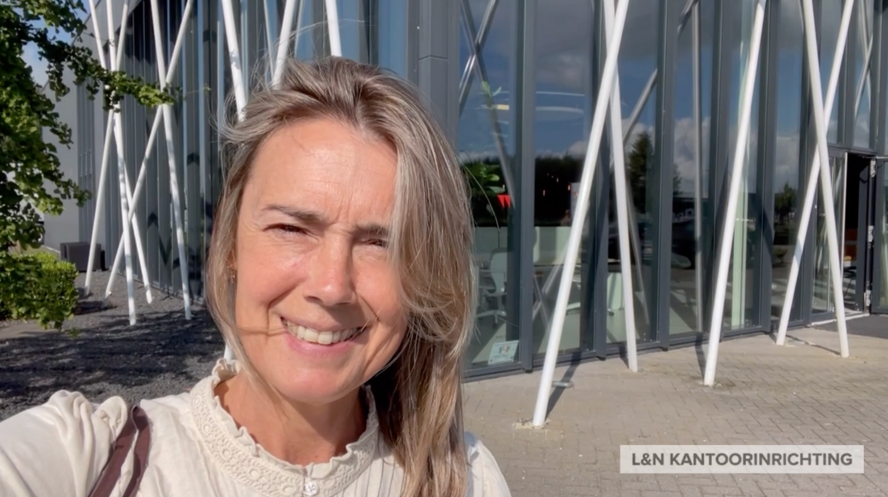 Vrouw voor modern kantoorgebouw met glazen gevel, buiten bij L&N Kantoorinrichting.