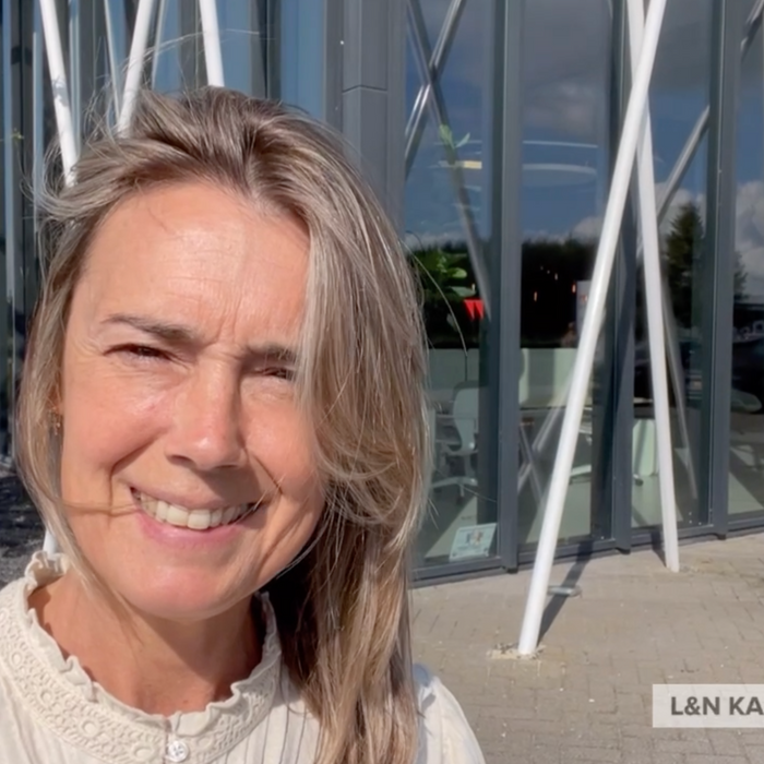 Vrouw voor modern kantoorgebouw met glazen gevel, buiten bij L&N Kantoorinrichting.