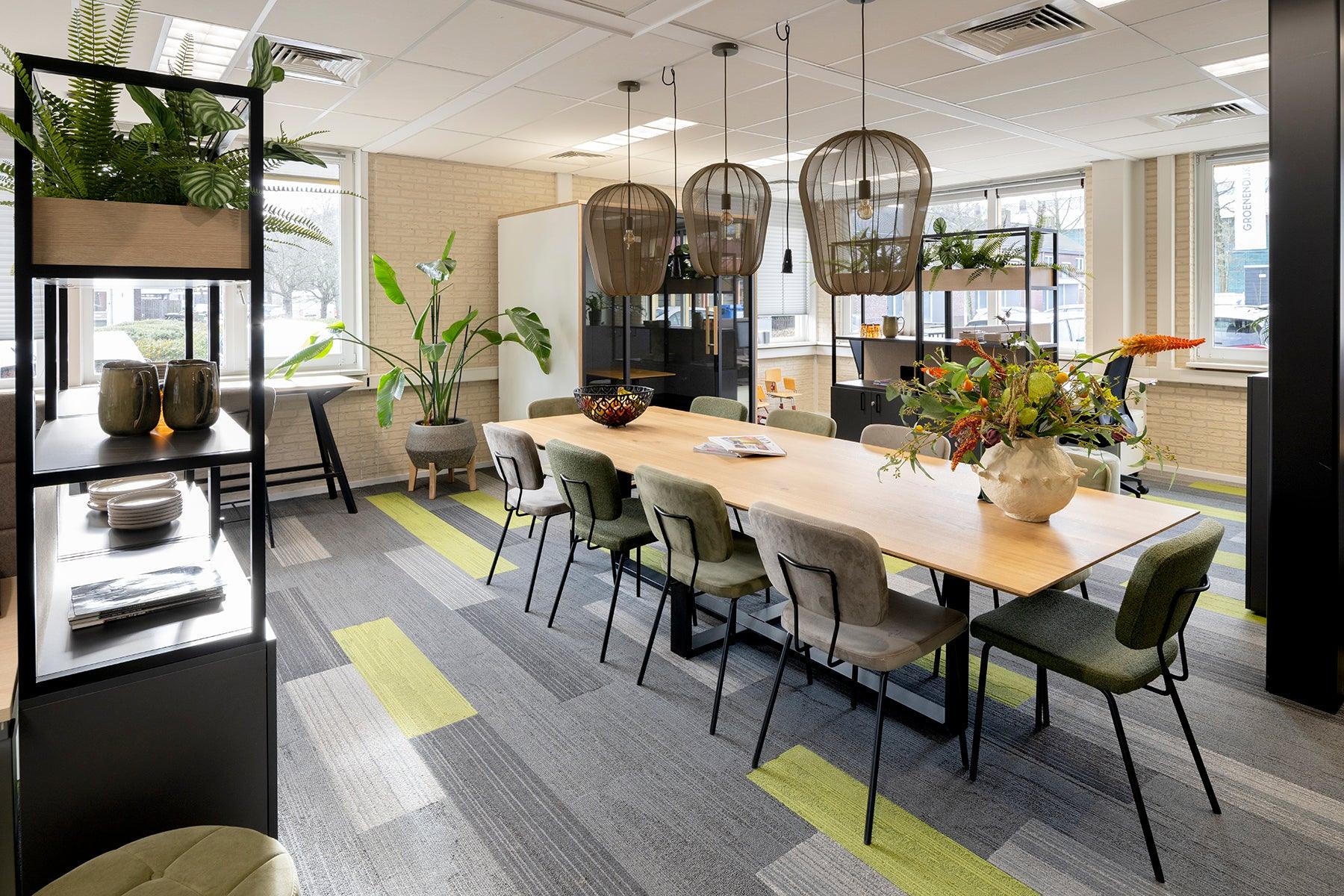 Moderne vergaderruimte met design kantoormeubilair, grote houten tafel en groene accenten.