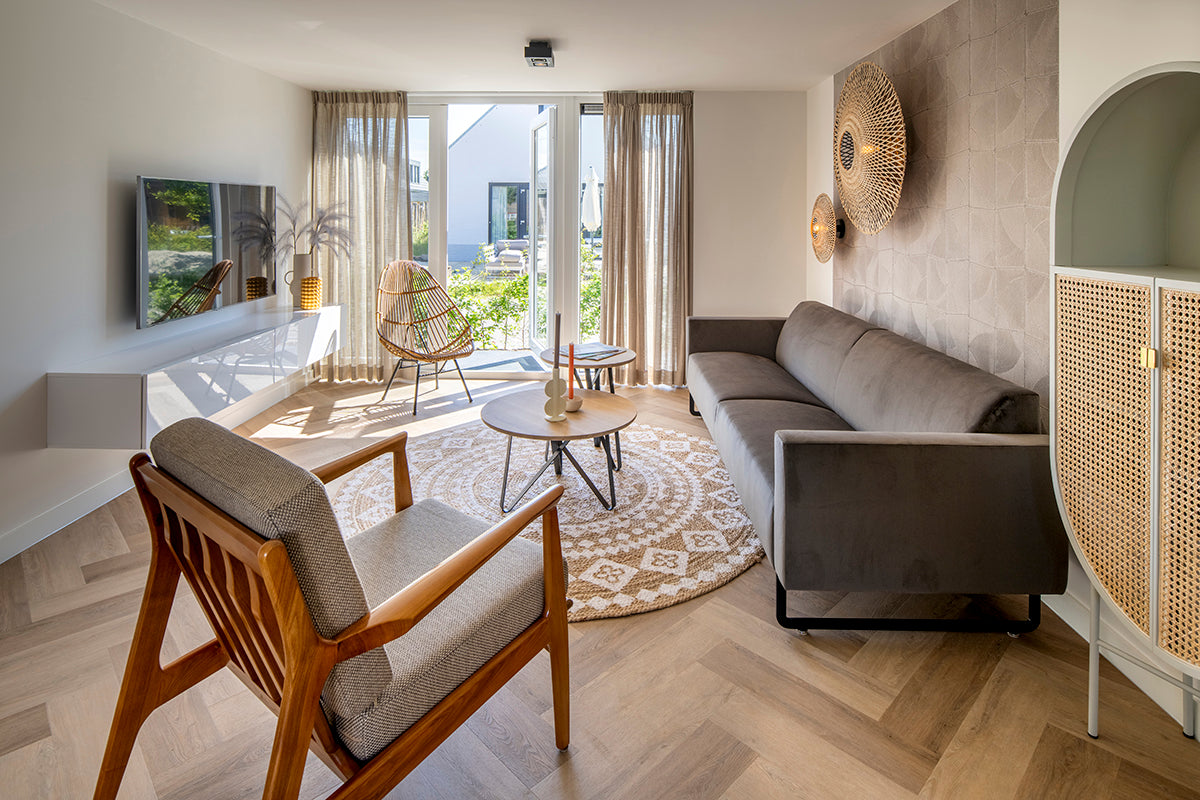 Modern ingerichte woonkamer met design bank, houten stoel en ronde salontafel, veel lichtinval