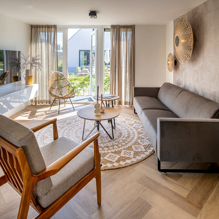 Modern ingerichte woonkamer met design bank, houten stoel en ronde salontafel, veel lichtinval