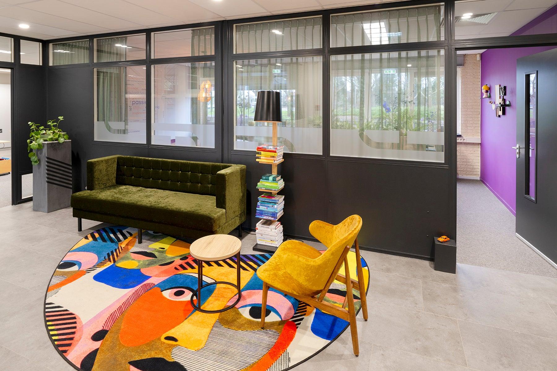 Moderne kantoorinrichting met design bank, gele stoel, kleurrijk vloerkleed en glazen wanden