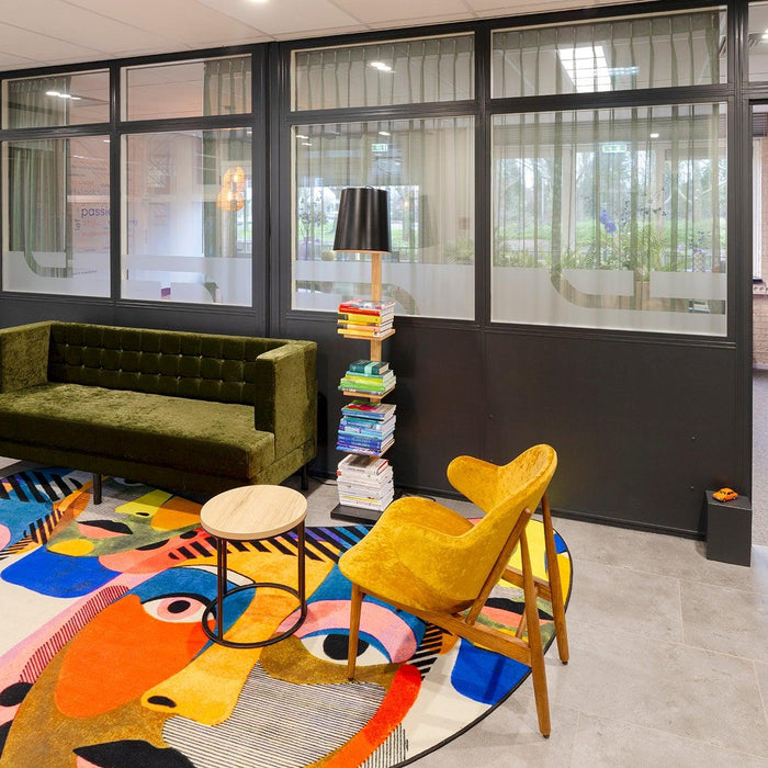 Moderne kantoorinrichting met design bank, gele stoel, kleurrijk vloerkleed en glazen wanden