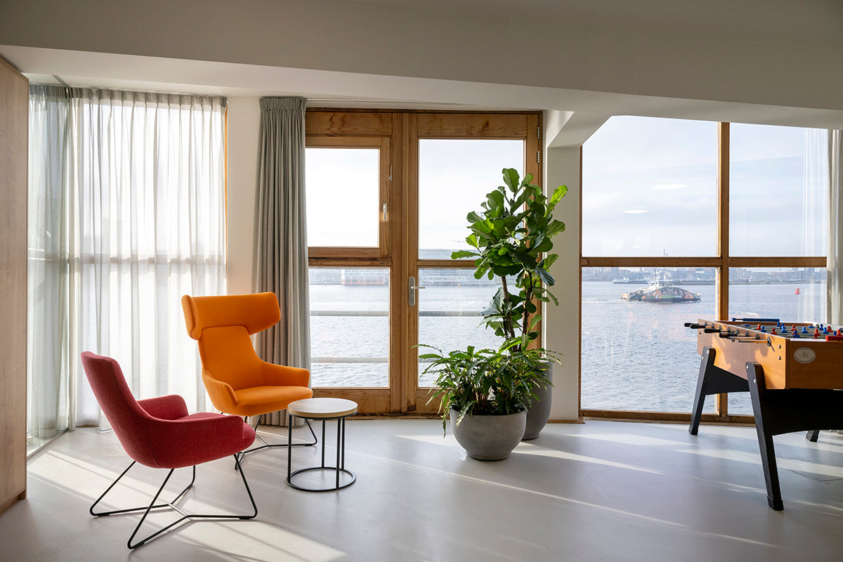 Moderne kantoorruimte met design kantoormeubels, lounge stoelen, planten en tafelvoetbal, uitzicht op het water