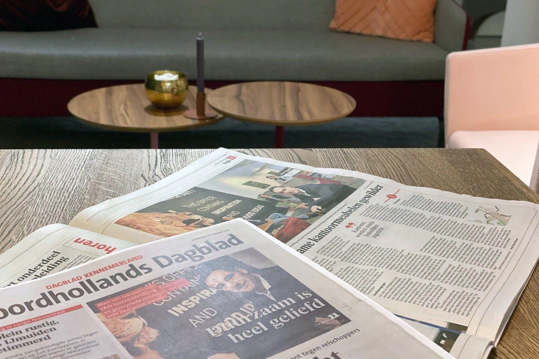Kranten op houten tafel in moderne kantoorruimte met designmeubels en loungehoek