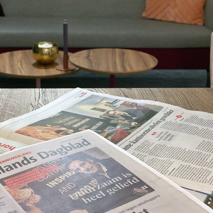 Kranten op houten tafel in moderne kantoorruimte met designmeubels en loungehoek