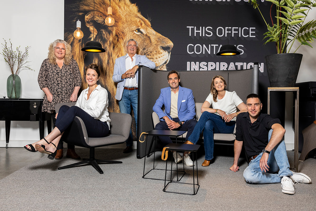 Teamfoto van KANTOORMEUBELS.ONLINE in moderne kantoorruimte met designmeubilair, leeuw muurdecor en inspirerende tekst.