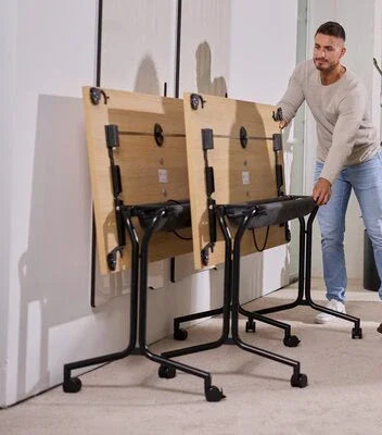 Man schuift inklapbare vergadertafels met wielen tegen muur, modern kantoormeubilair