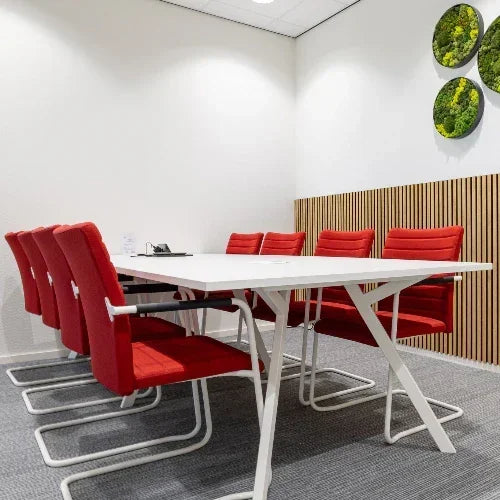 Moderne vergaderruimte met witte Bridge vergadertafel, rode Alfa stoelen met hoge rug en groene muurdecoratie, moswand, kantoormeubilair