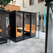 Akoestische vergaderruimte met oranje banken en glazen deuren in modern kantoor.