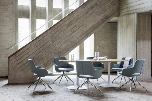 Artifort Clarion tafel met zes Jima stoelen met chromen spinvoet onderstel en lichtblauwe stoffering, in een industriële ruimte met een betonnen trap en hoge ramen op de achtergrond