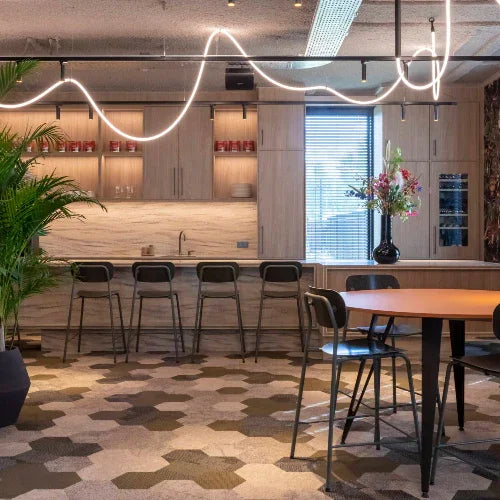 Moderne kantoor keuken met houten kasten, barkrukken, design tafel en bloemdecoratie.