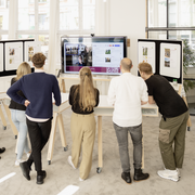 5 personen volgen een videomeeting op grote monitor - WHAT IF WE FLY - teamdesk, teambord, monitor on wheels, Interstuhl 