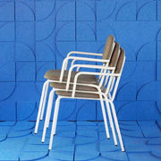 Stapelbare design armstoelen met witte poten voor kantoor, tegen blauwe wand.