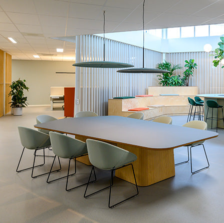 Moderne vergadertafel met groene designstoelen in lichte kantoorruimte, kantoormeubels online