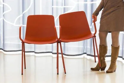 Vrouw koppelt twee rode zaalstoelen met armleuning in moderne kantoorruimte bij Kantoormeubels.online