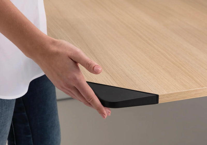 Hand houdt hoek van modern houten bureau met zwarte poot, design kantoormeubilair