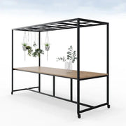 Moderne houten vergadertafel met zwart metalen frame, rooster en planten, op wielen.