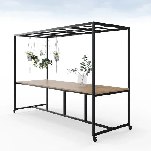 Moderne houten vergadertafel met zwart metalen frame, rooster en planten, op wielen.