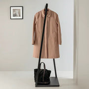 Staande design kapstok met beige jas en zwarte tas, modern kantoorinterieur