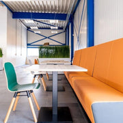 Moderne kantoormeubels met oranje bank, groene stoel en kolomtafels in lichte werkruimte