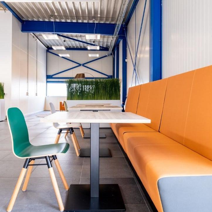 Moderne kantoormeubels met oranje bank, groene stoel en kolomtafels in lichte werkruimte