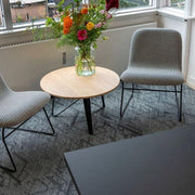 Twee moderne loungestoelen bij ronde houten tafel met bloemenvaas in kantoorruimte