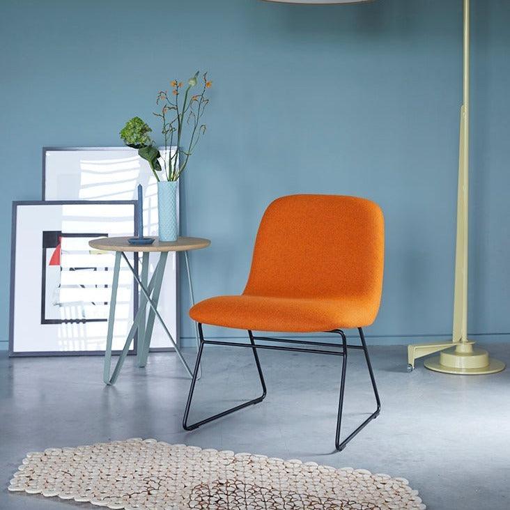 Design loungestoel in oranje stof met metalen frame, bijzettafel en kunst aan muur, kantoormeubels