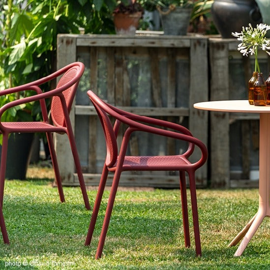 rode Pedrali Remind stoelen met armleggers, op een buitenterras met gras ondergrond