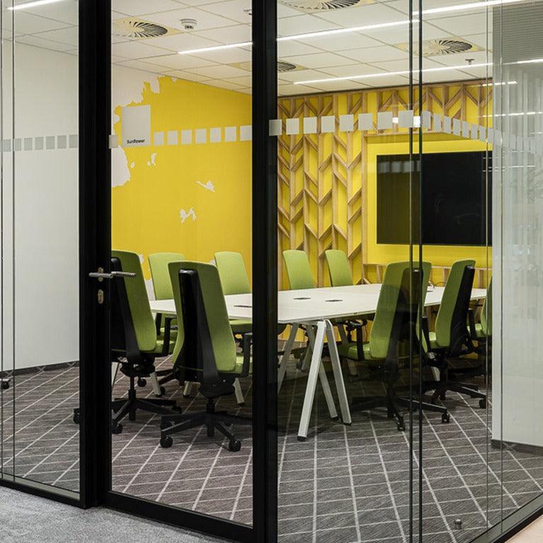Moderne vergaderruimte met design bureaustoelen, gele accentmuur en glazen wanden.