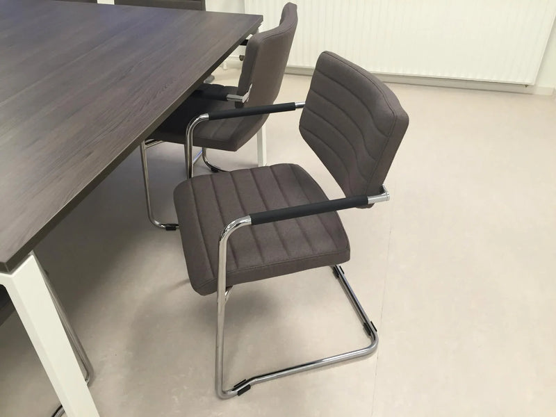 Design vergaderstoel Alfa sledemodel met lage rug, grijze stof en metalen frame bij kantoortafel.