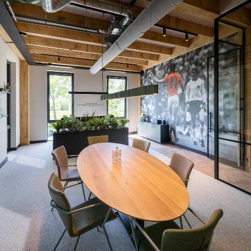 Moderne vergaderruimte met ovale houten tafel, design bureaustoelen en groene kantoorplanten