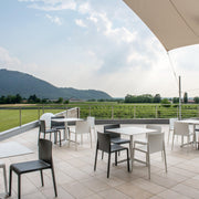 Moderne design buitenstoelen en -tafels op een terras met uitzicht op groene velden en heuvels.