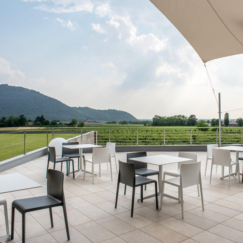 Moderne design buitenstoelen en -tafels op een terras met uitzicht op groene velden en heuvels.