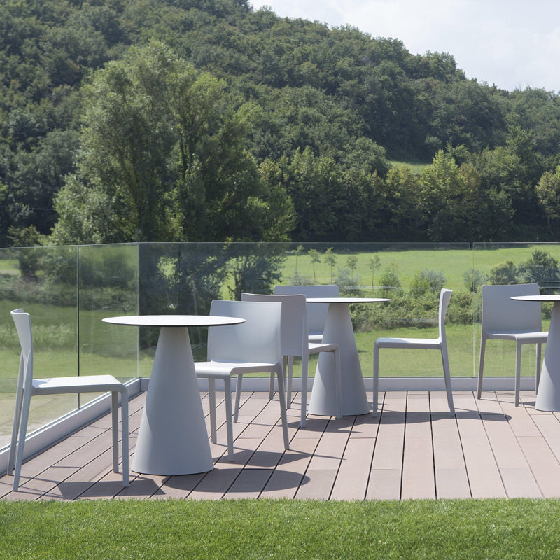 Moderne witte design stoelen en ronde tafels buiten op terras, uitzicht op groen landschap.