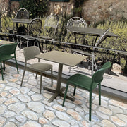Buitenterras met op de voorgrond vierteens tafel Fermoni en Gaber Haily stoelen (zonder armleggers), uitgevoerd in de kleuren zand en groen.
