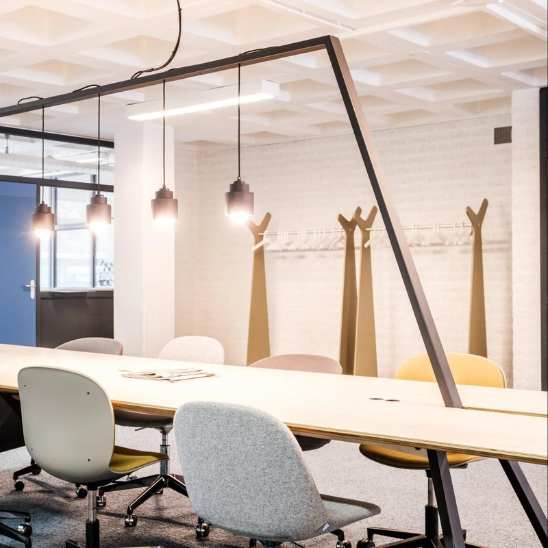 Moderne vergadertafel met design bureaustoelen, hanglampen en kapstokken in kantoorruimte