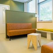 Design treinbank in kantoorruimte met bruine bank, houten bijzettafel en groene wand.