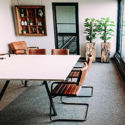 Moderne Bridge vergadertafel met leren Alfstoelen, planten en houten decor in kantoorruimte 