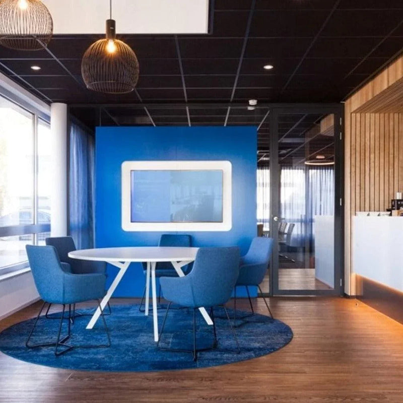 Bridge ronde tafel met wit blad en wit frame, met blauwe stoelen in moderne kantoorruimte, houten vloer, blauwe accentmuur.
