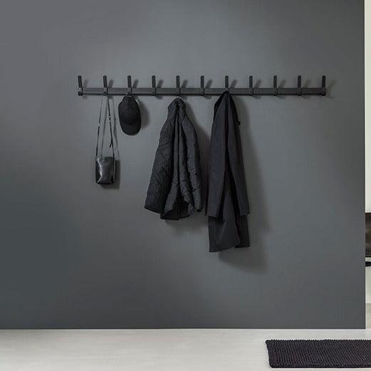 Zwarte wandkapstok met jassen, tas en pet in modern kantoorinterieur, kantoormeubels online