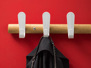 Design wandkapstok met houten stang, witte haken en zwarte tas tegen rode muur, kantoormeubilair